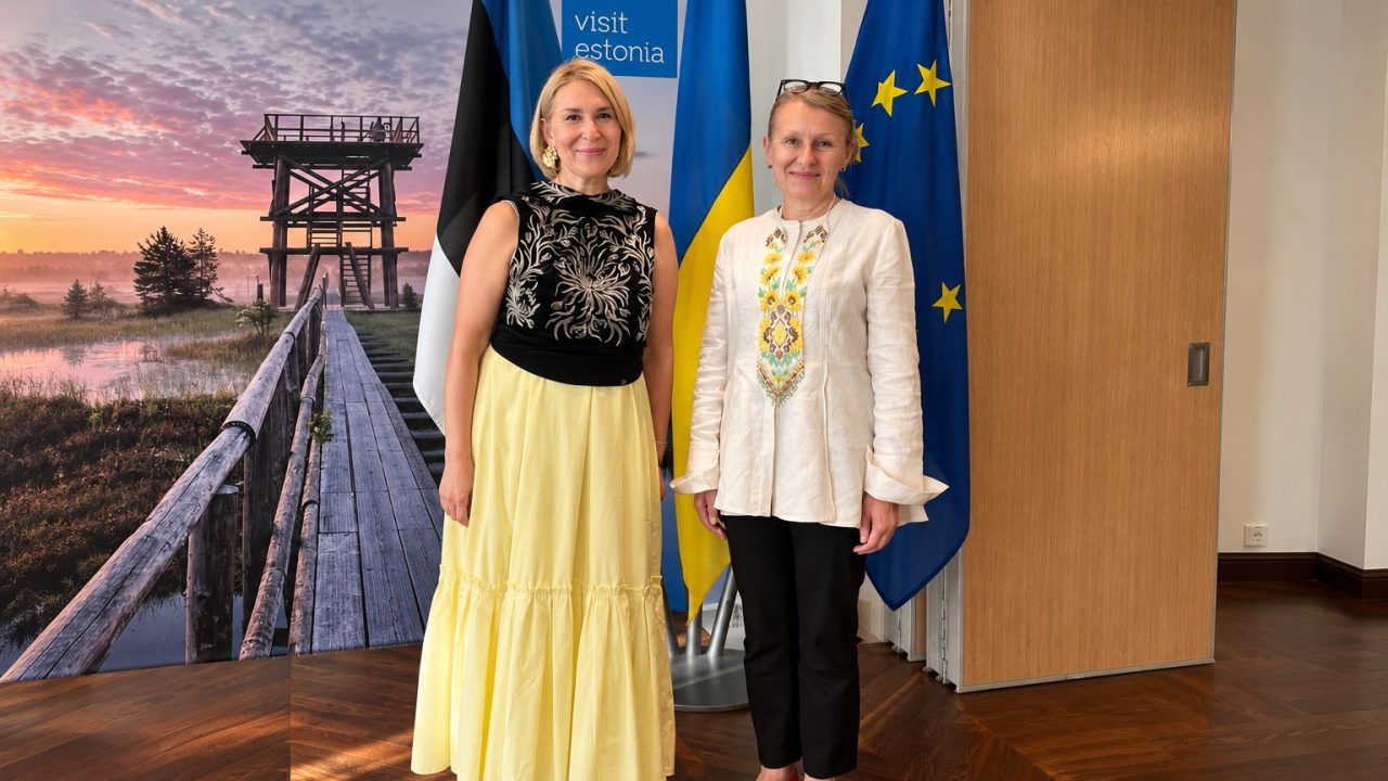 Дві жінки стоять на тлі прапорів Естонії, України та Євросоюзу