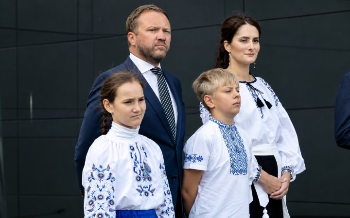 Учасники церемонії підняття прапора у Таллінні: чоловік у темному костюмі, двоє дітей і жінка у вишиванках